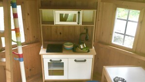 A small kitchen with a microwave, sink, and a window. There is a colorful rug and a stool.