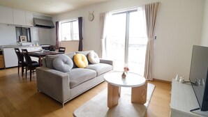 Un salon moderne avec un canapé gris, une table basse ronde et un téléviseur posé sur un meuble.