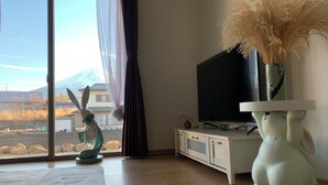 Une pièce dotée d’une grande fenêtre, d’un téléviseur posé sur un meuble et d’une statuette de lapin décorative.