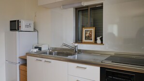 Une cuisine compacte équipée d’un micro-ondes encastré, d’un évier et d’une fenêtre ornée d’un tableau.