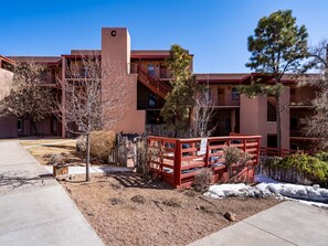 A multi-story building with a red exterior and a central staircase. There are trees and shrubs in the foreground, and a clear blue sky in the background. - Casa Cielo | Great Location + Southwest Condo (Santa Fe)