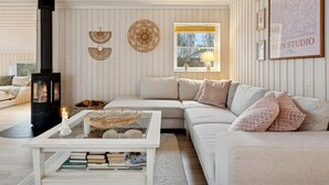 Ein gemütliches Wohnzimmer mit einem weißen Sofa, einem Glastisch, einem schwarzen Kamin und einem Fenster mit Blick auf Bäume.