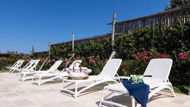 A row of white lounge chairs with a wooden fence and lush greenery in the background. - Clivia- 03 bedroom villa with private terrace (Massa Lubrense)