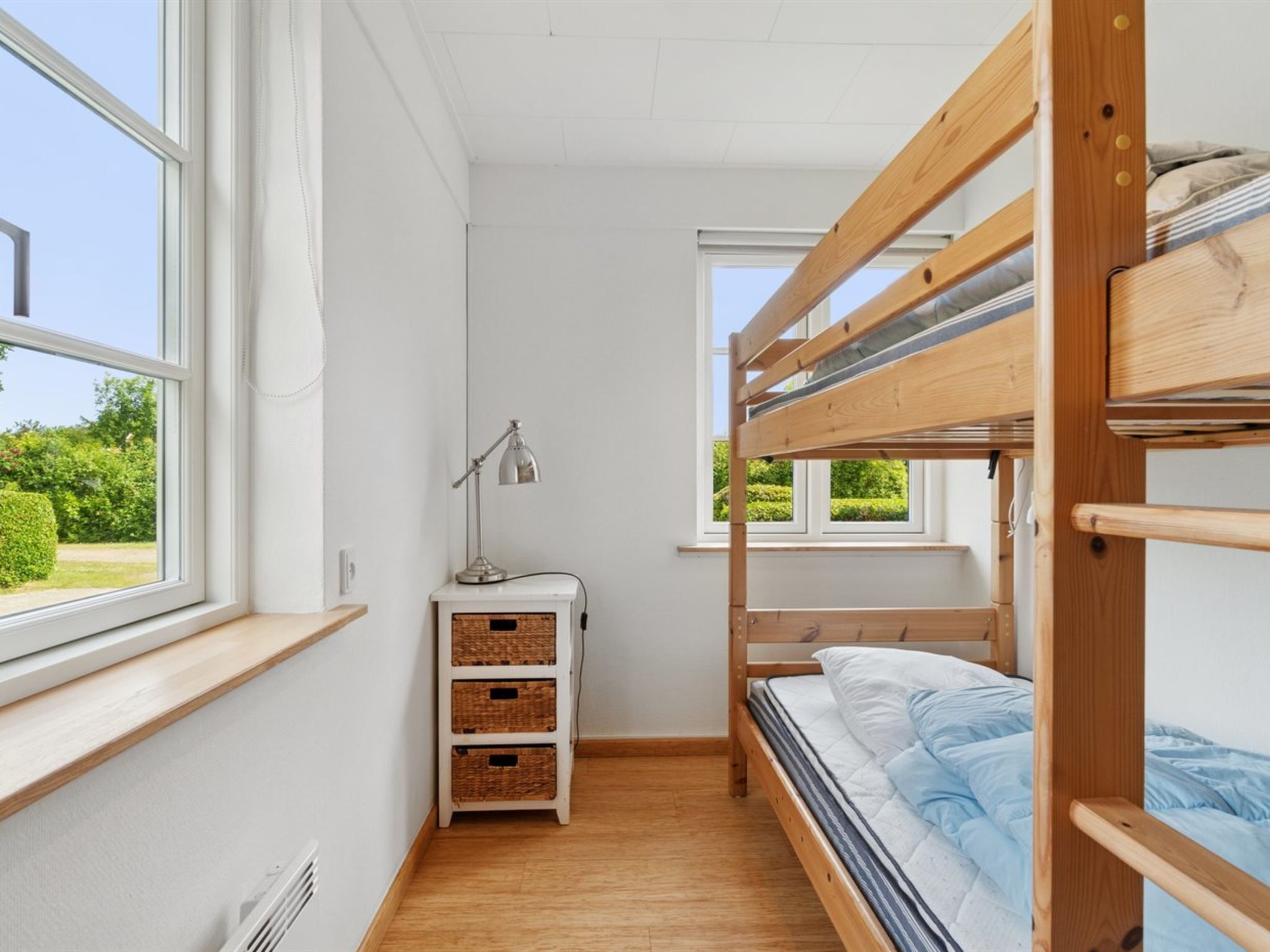 A compact room with bunk beds, a desk with a lamp, and a window overlooking greenery.