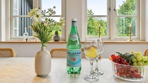 Ein Tisch mit einer Pellegrino-Flasche, einem Blumenstrauß in einer Vase, zwei Gläsern mit Zitronenscheiben und einer Schale Trauben.