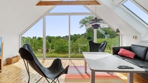 Ein modernes Loft mit schrägedach, großen Fenstern, einem Essbereich mit Tisch und Stühlen sowie einer Couch mit rotem Kissen.