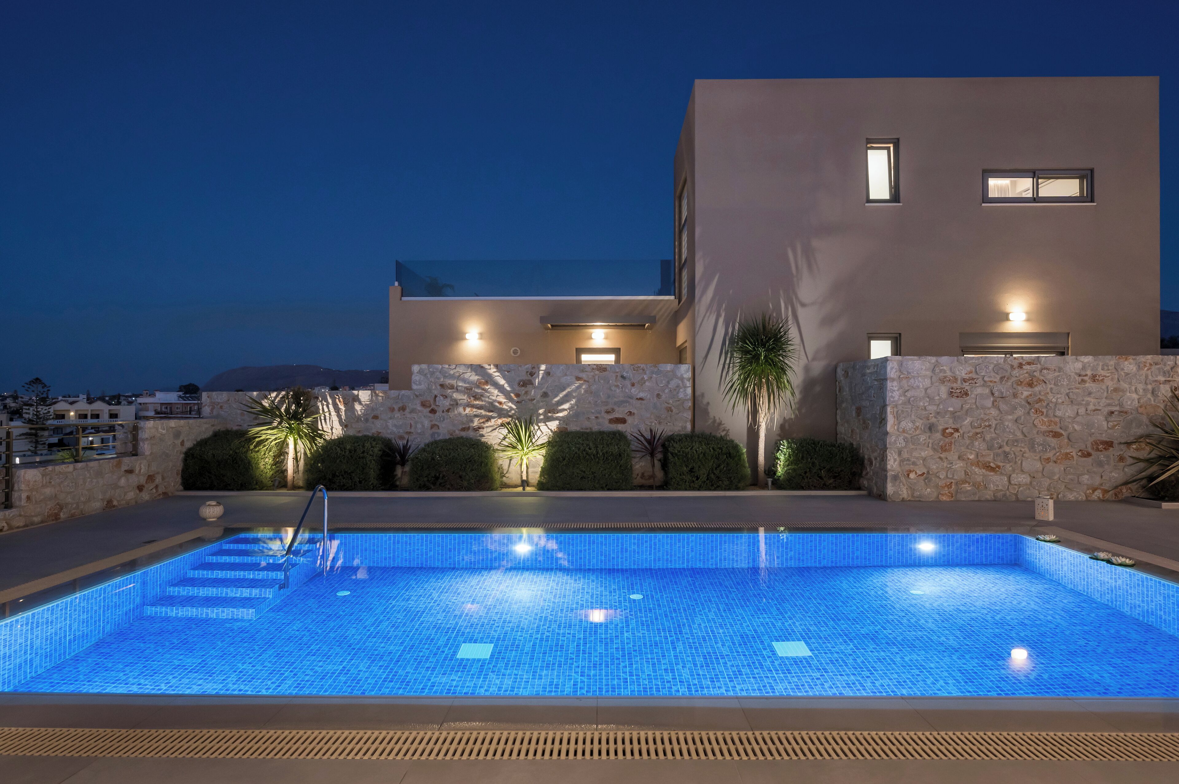 A modern building with a swimming pool, stone walls, and outdoor lighting.