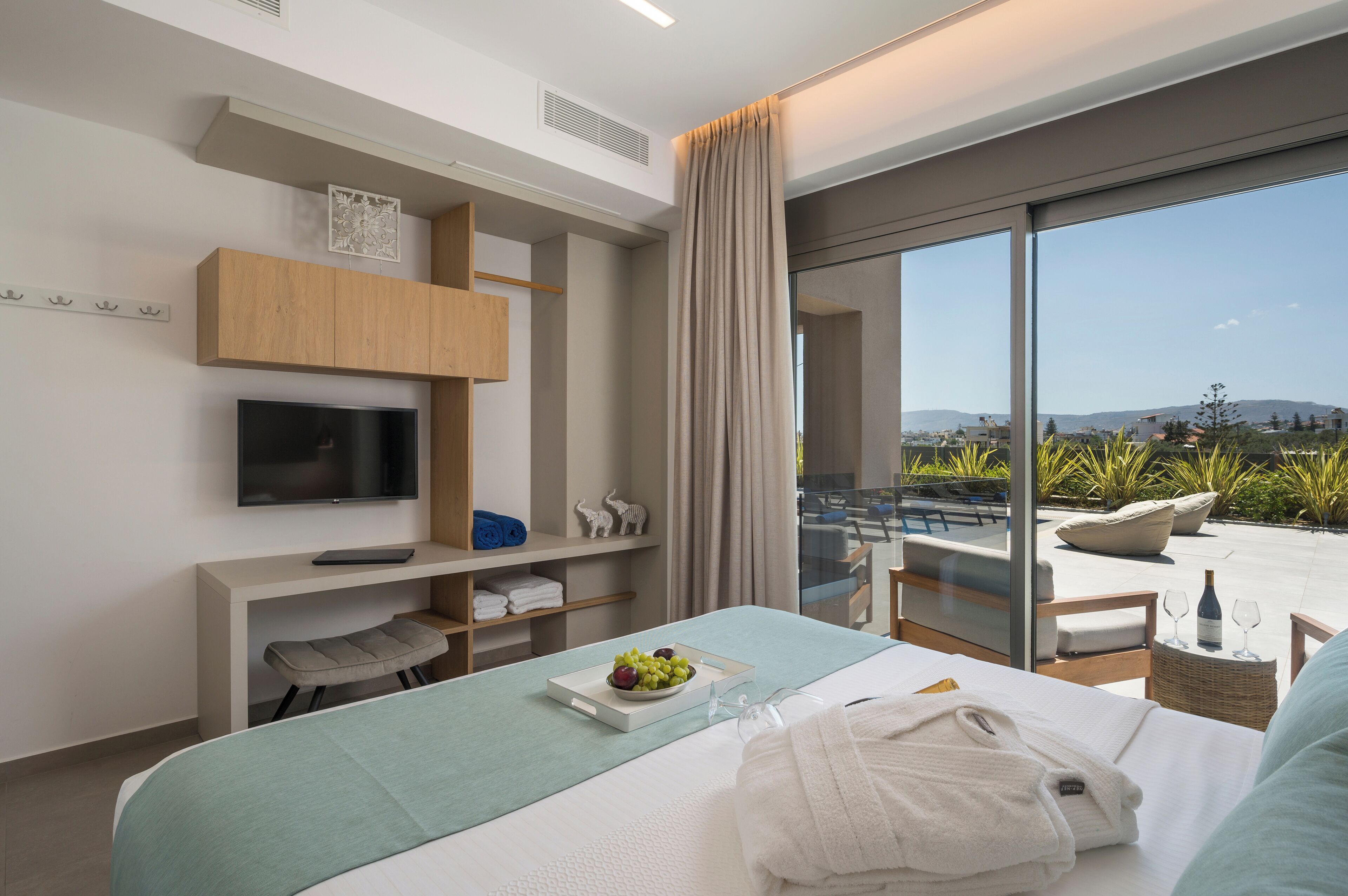 A modern hotel room with a bed, a TV, a desk, and a balcony with a view of the landscape.