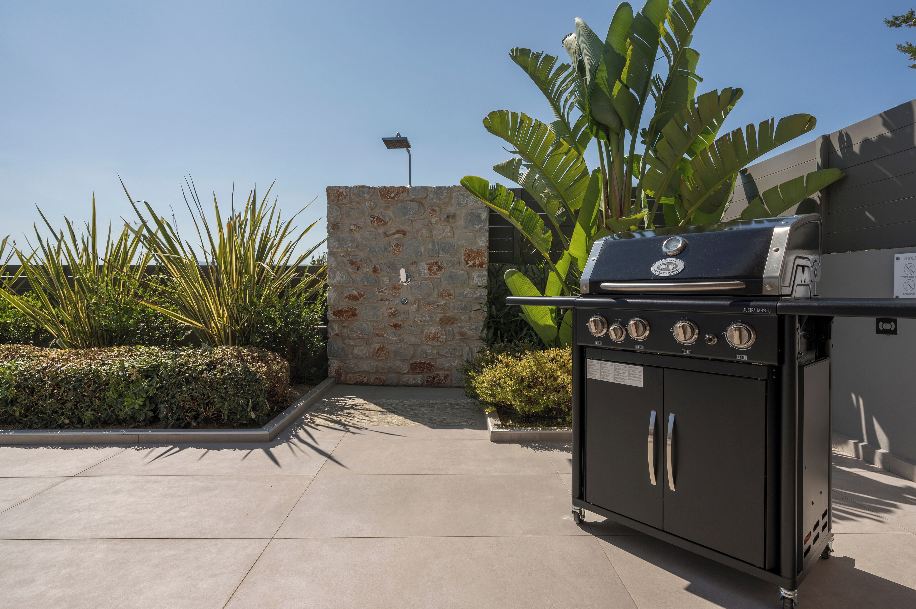 An outdoor barbecue area with a stone wall, a large green plant, and a black grill station.