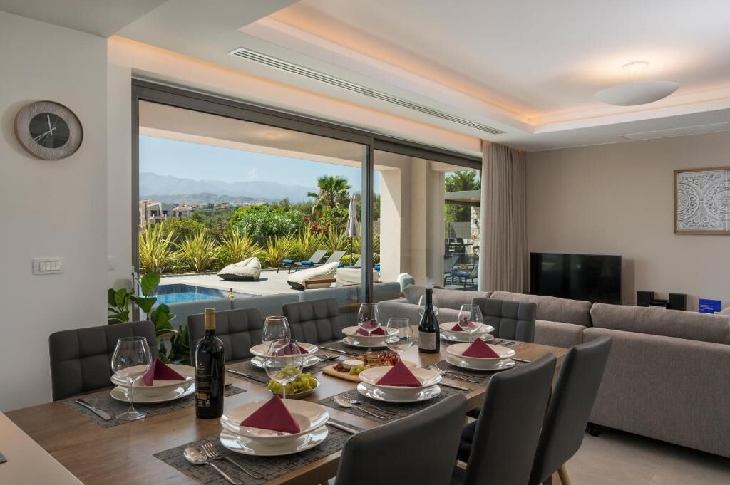 Un coin repas avec une table dressée pour six personnes, une vue sur la piscine, et un espace de détente avec un canapé et un téléviseur.