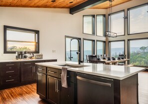 A modern kitchen with a large island, dark cabinetry, and a view of the outdoors through multiple windows. - Indoor Pool Cabin w/ Views, Theater & Hot Tub (Sevierville)