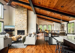 A spacious living area with a stone fireplace, wooden floors, and large windows offering views of the outdoors. - Indoor Pool Cabin w/ Views, Theater & Hot Tub (Sevierville)