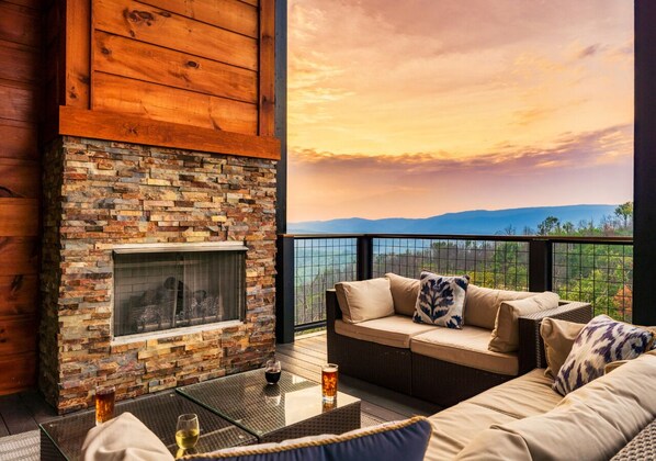 A cozy outdoor seating area with a stone fireplace, a cushioned sofa, and a glass table. - Indoor Pool Cabin w/ Views, Theater & Hot Tub (Sevierville)