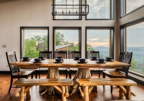 A dining area with a large wooden table and chairs, large windows with a view of trees and mountains, and a hanging light fixture. - Indoor Pool Cabin w/ Views, Theater & Hot Tub (Sevierville)