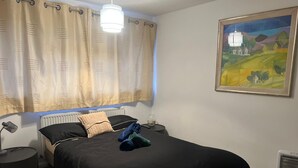 Een slaapkamer met een zwart bed, beige gordijnen, een schilderij aan de muur en een radiator.