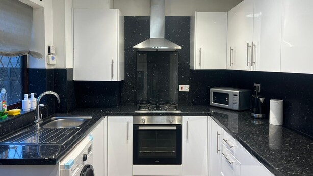 Een moderne keuken met witte kastjes, een zwart aanrecht, een roestvrijstalen afzuigkap, een magnetron en een vaatwasser.