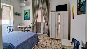 Een kamer met een bed, een bureau, een stoel, een kledingkast en een raam met gordijnen.