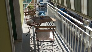 Een balkon met een tafel en stoelen, een leuning, en zicht op geparkeerde auto’s en gebouwen op de achtergrond.