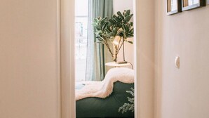 A narrow hallway with wooden flooring leading to a room with a green sofa, a small table, and a potted plant. - Saudade Apartment (Lisbon)