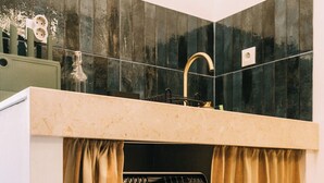 A compact laundry room with a front-loading washing machine, a sink with a gold faucet, and a tiled backsplash. - Saudade Apartment (Lisbon)
