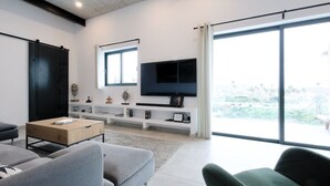 Ein modernes Wohnzimmer mit großem Fenster, einem wandmontierten Flachbildfernseher und minimalistischem Design.