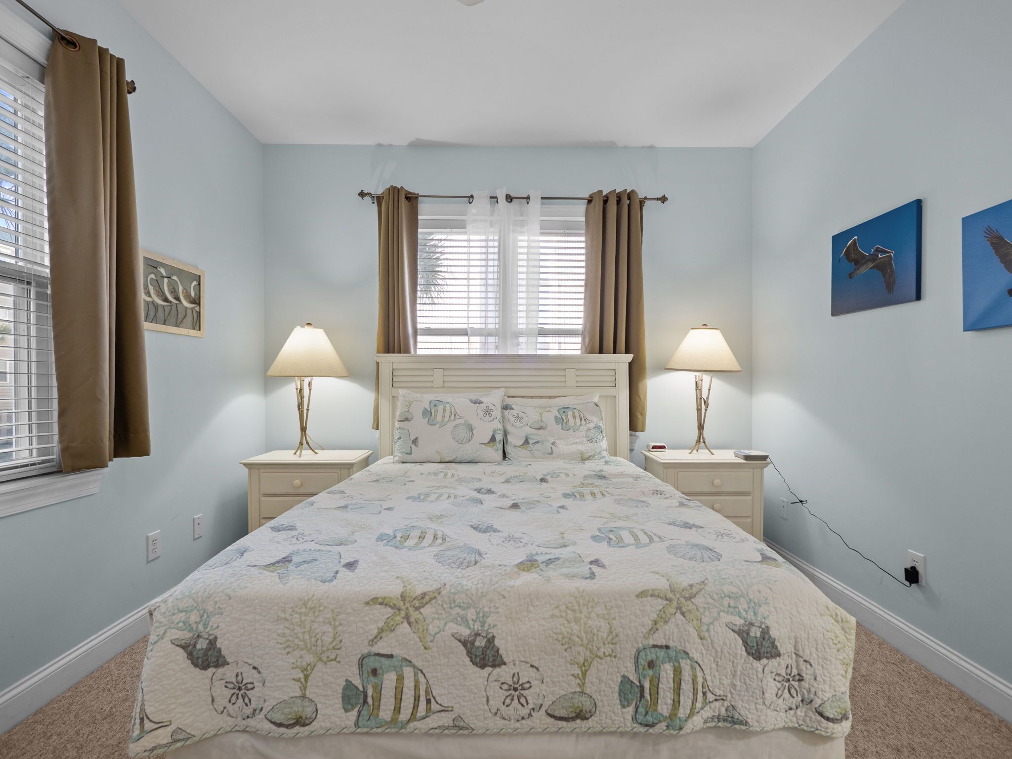 Une chambre à coucher avec un lit, deux lampes de chevet, une fenêtre avec des rideaux et des œuvres d’art murales.