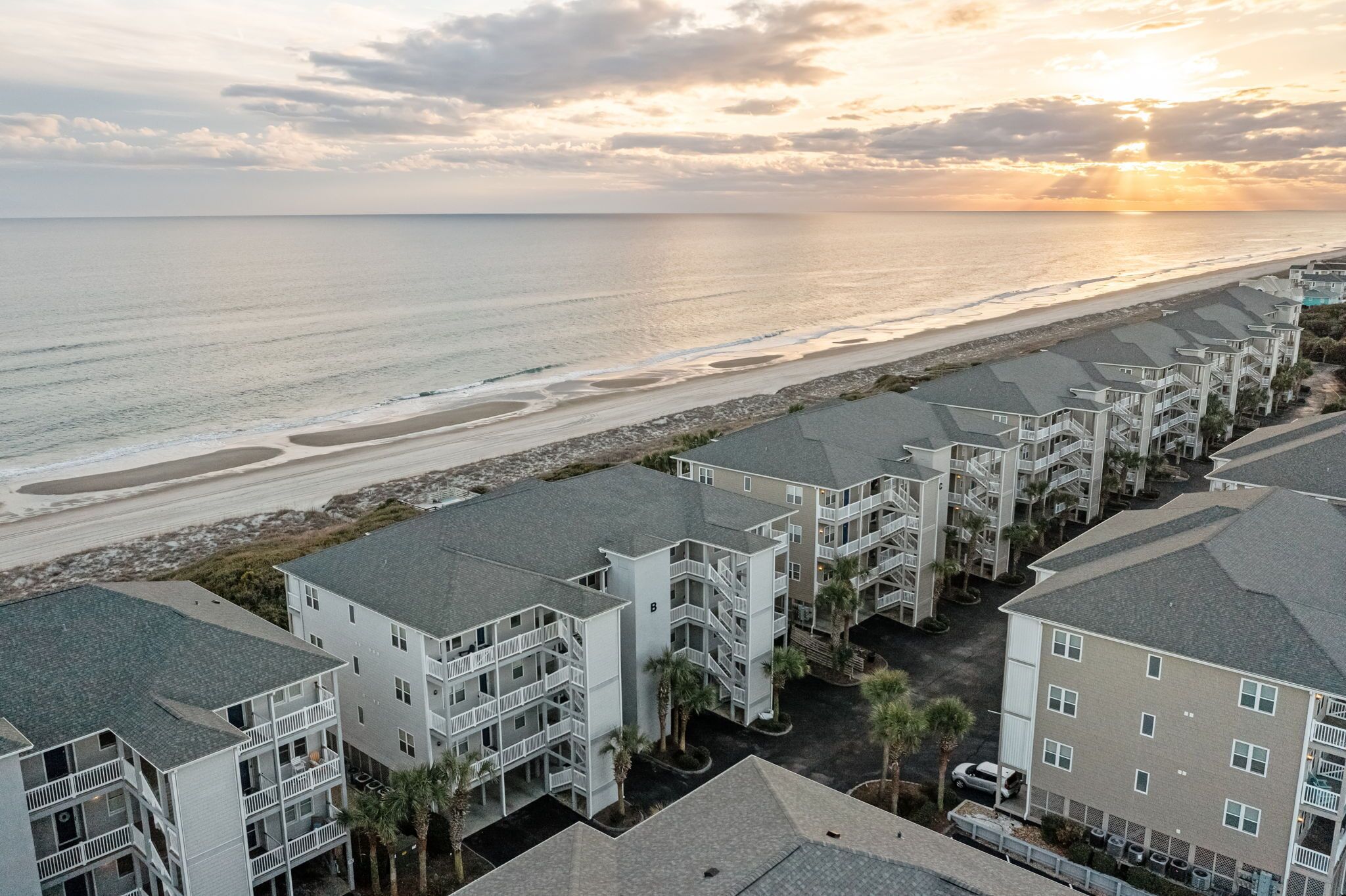 A beachfront hotel with multiple-story buildings, a parking area, and a view of the ocean.
