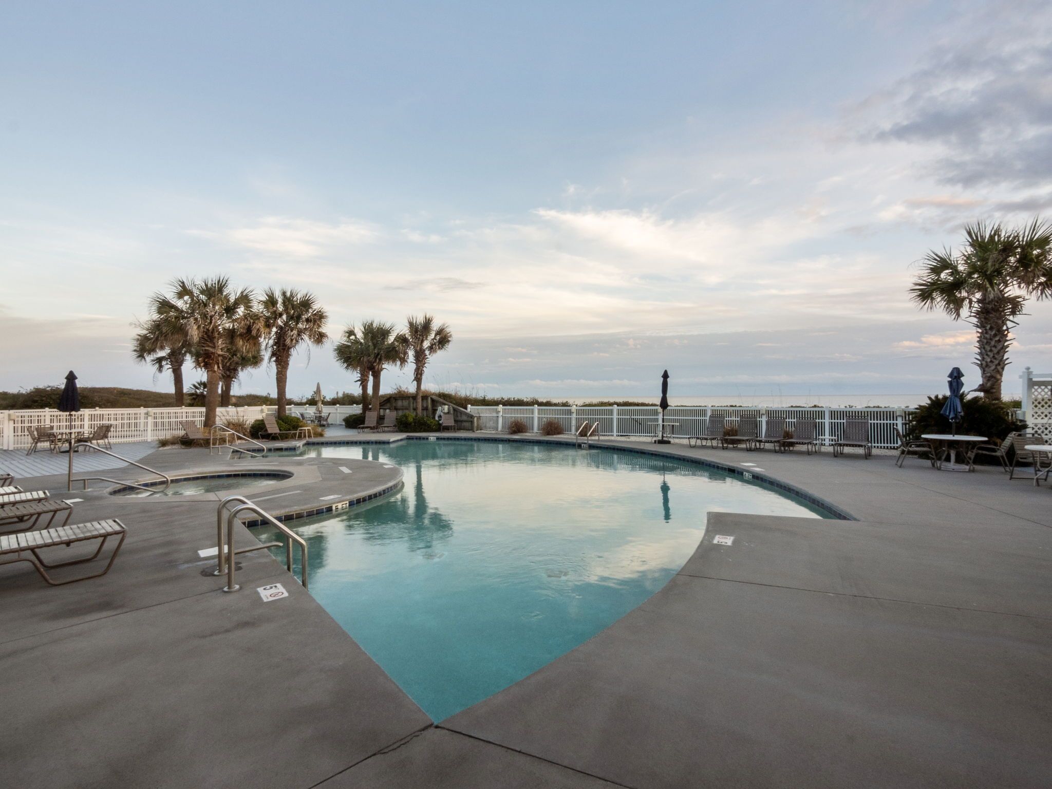 A swimming pool with a deck, lounge chairs, and palm trees.