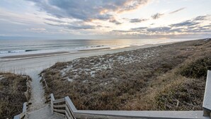 En strand med en träpromenad som leder ner till stranden, sanddyner och en molnig himmel.