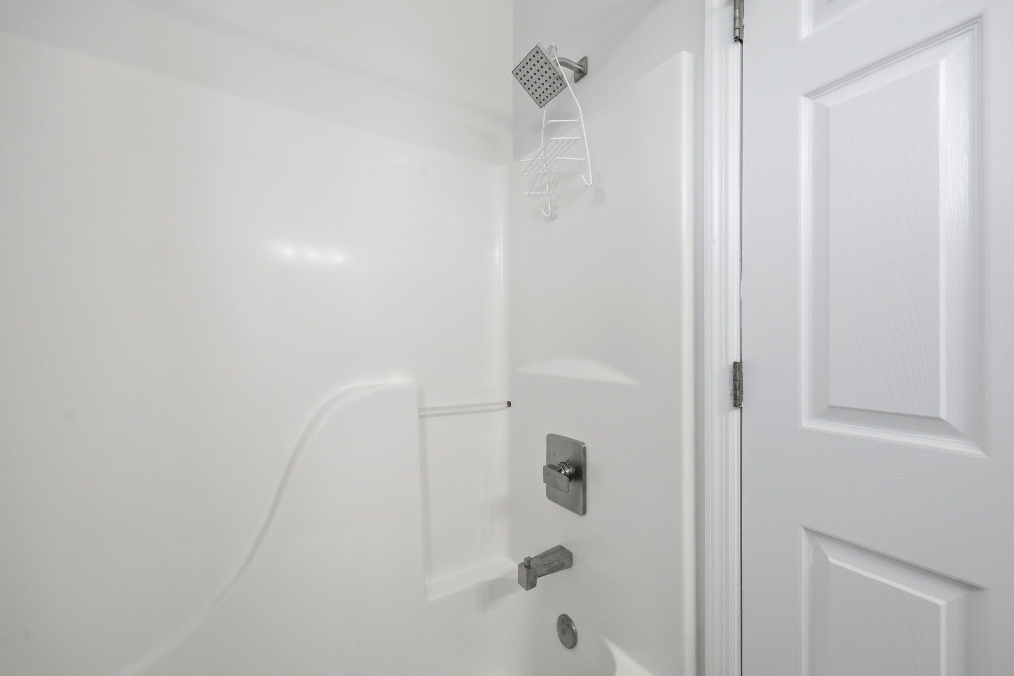 A white shower with a handheld showerhead, a wall-mounted control panel, and a door with a handle.