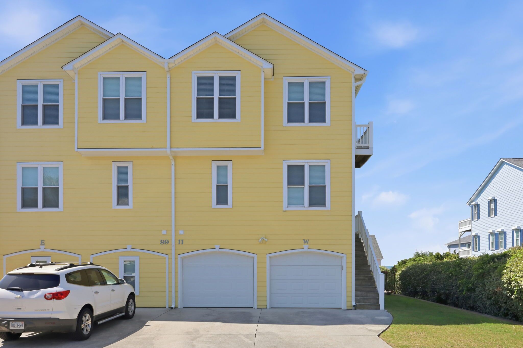Un immeuble résidentiel jaune, à plusieurs étages, avec deux garages, un escalier et un ciel dégagé.