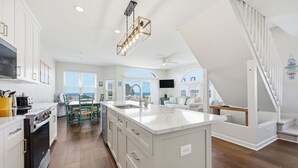 Una cucina moderna con mobili bianchi, un'isola centrale e un'area pranzo con sedie verdi.
