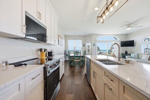 A modern kitchen with a large island, built-in oven, and a dining area with a view. - Beach Allure West | Pet-Friendly Oceanfront Duplex (Emerald Isle)