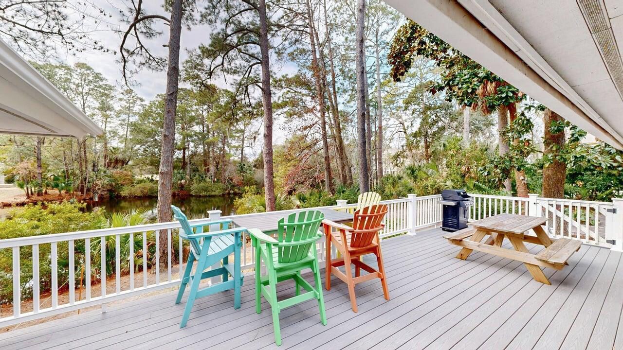 Une terrasse en bois avec une balustrade blanche, trois chaises Adirondack et une table de pique-nique.