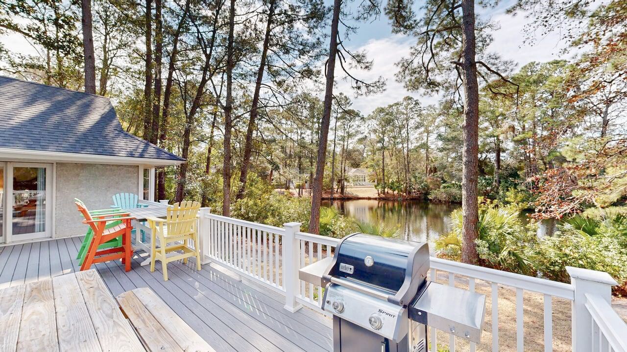 Une terrasse équipée d’un barbecue, de chaises et offrant une vue sur un lac entouré d’arbres.