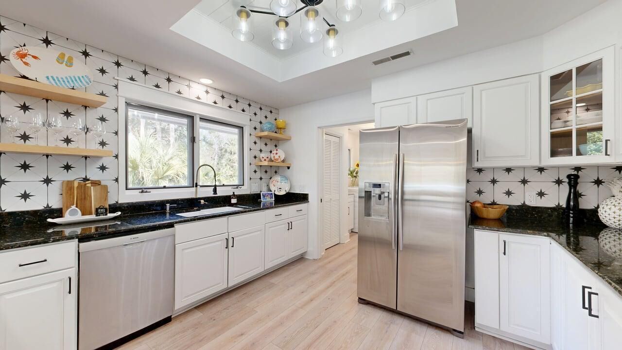 A modern kitchen with white cabinets, a stainless steel refrigerator, and a black countertop.