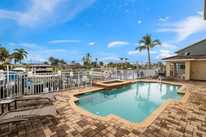 A swimming pool with a tiled deck, lounge chairs, and palm trees in the background. - 3 bed- 2 bath Condo - community pool and hot tub (Cape Coral)
