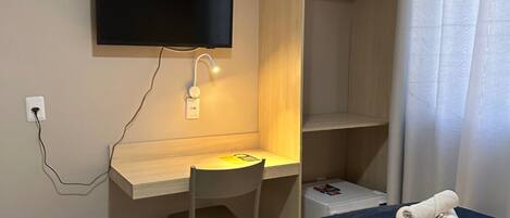 Una habitación con una cama, un escritorio con silla, un televisor montado en la pared y una mesita con toallas.