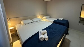 Een hotelkamer met twee bedden, elk voorzien van witte lakens en een donkerblauwe sprei. Twee nachtkastjes met lampen, en een klein tafeltje met een lamp in de hoek.
