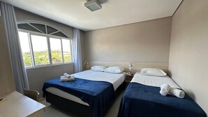 Een hotelkamer met twee bedden, een bureau en een raam met gordijnen.