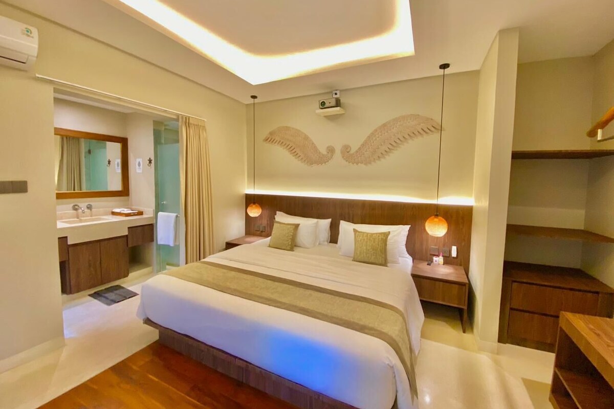 Une chambre d’hôtel moderne dotée d’un grand lit, d’une coiffeuse avec miroir et d’un plafond orné de motifs ailés.