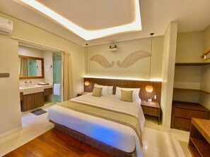 A modern hotel room with a large bed, a vanity with a mirror, and a ceiling with a winged design. - Baliris Home Boutique (Legian)