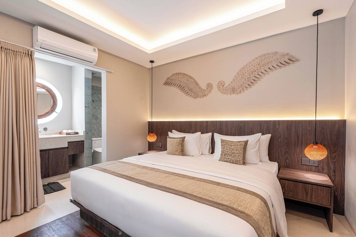 A modern hotel room with a large bed, a vanity with a mirror, and a wall-mounted air conditioner.