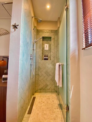 A shower with a herringbone tile pattern, a towel rack, and a sign with a running figure. - Baliris Home Boutique (Legian)
