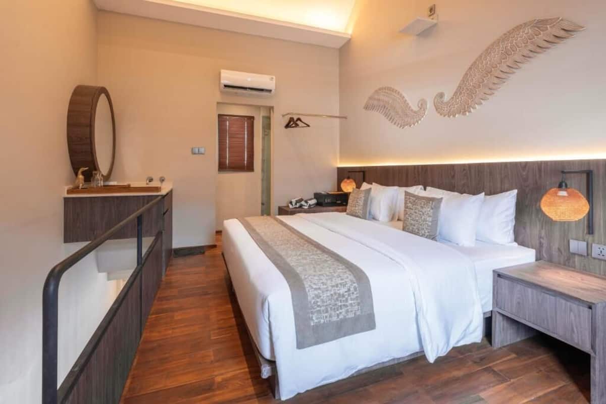 A hotel room with a large bed, a wooden headboard, a bedside table, a nightstand, a mirror, and a wall-mounted light fixture.