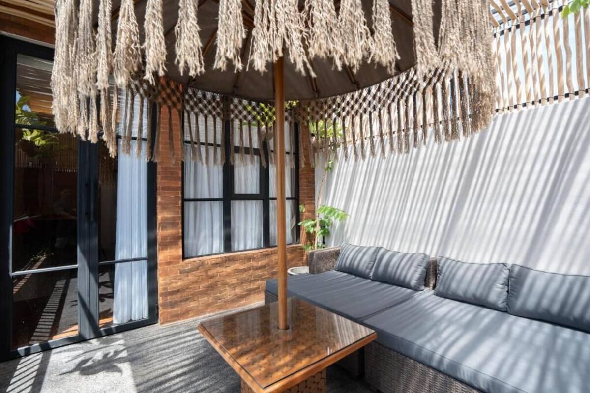 A modern outdoor seating area with a sofa, a wooden table, and a hanging macrame umbrella.