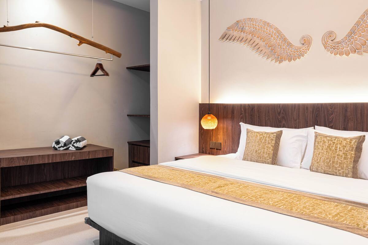 A modern hotel room with a large bed, wooden headboard, and a wall-mounted light fixture.