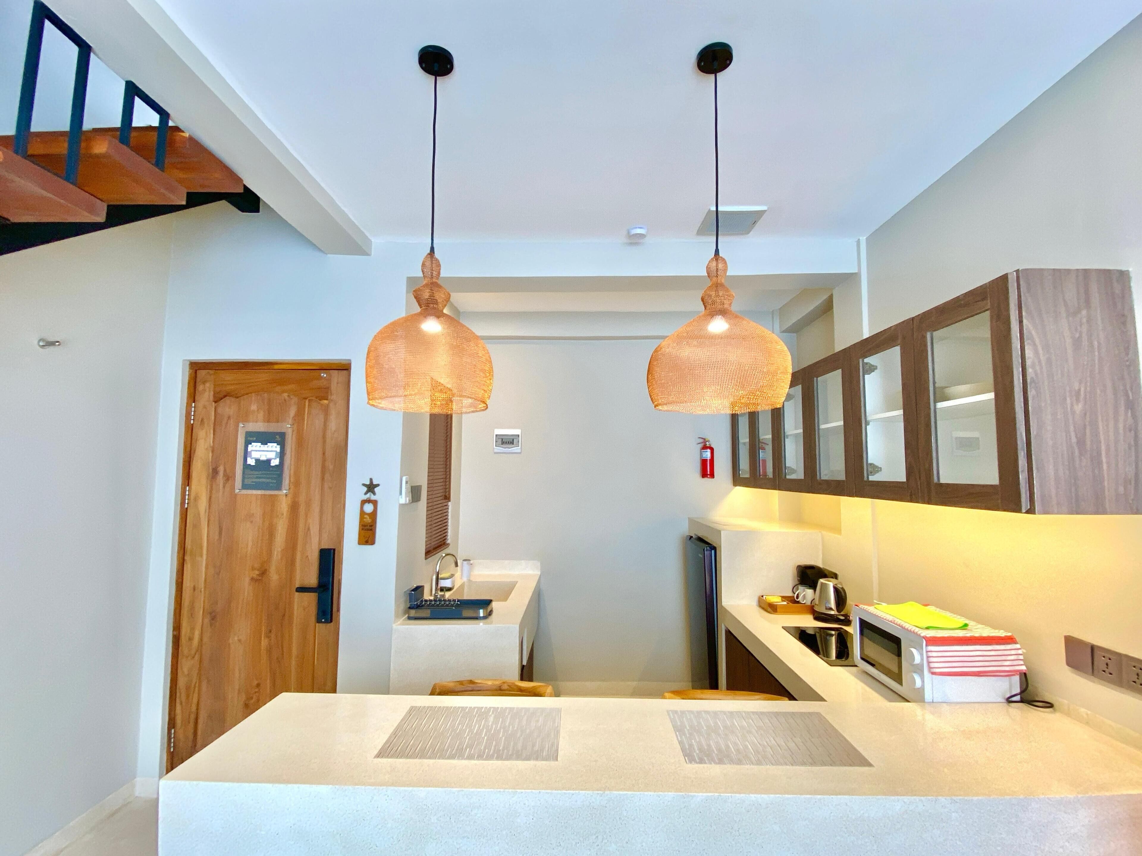 Una cocina moderna con una isla central, luces colgantes y una escalera de madera.