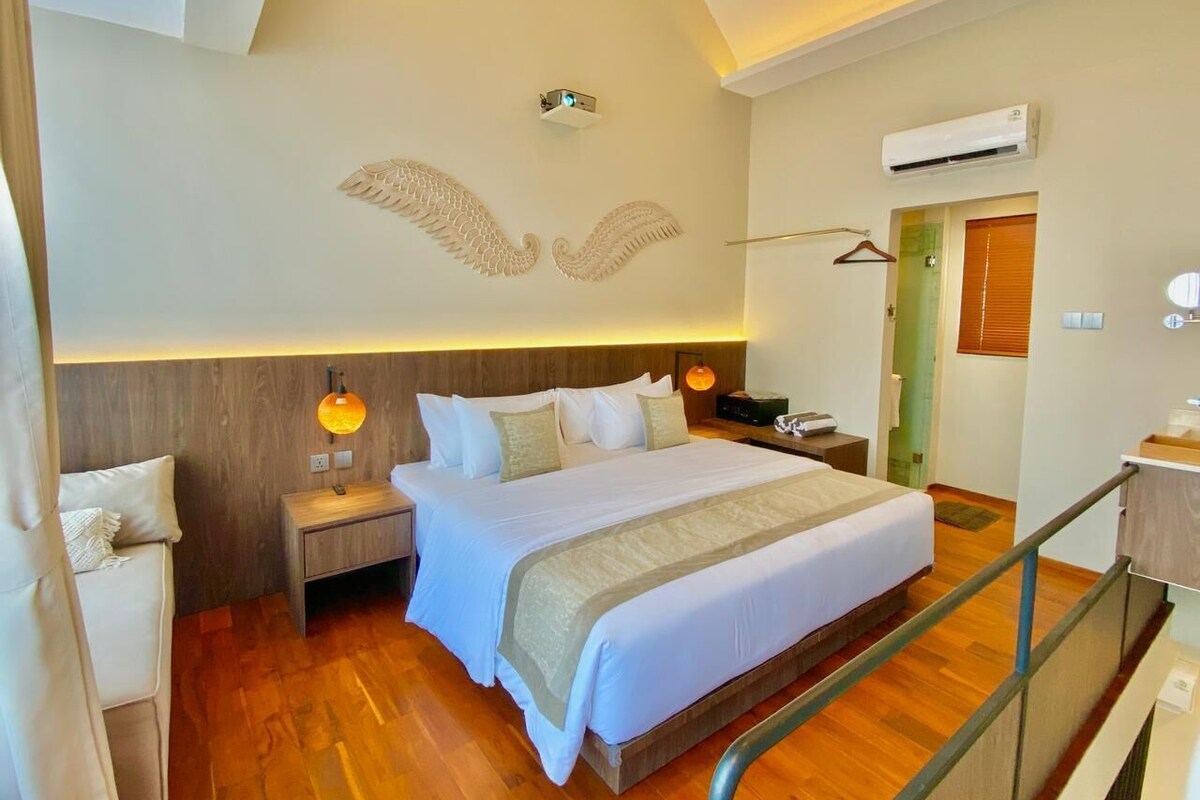 Une chambre d’hôtel avec un grand lit, des tables de chevet, un luminaire suspendu et un appareil de climatisation.