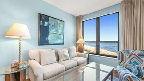 A modern living room with a beige sofa, two lamps, a glass coffee table, and a large window with a view of the beach. - Unit 0702E a beautiful 2 bedroom and 2 bath unit (ORANGE BEACH)